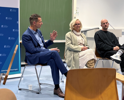 Drei Menschen sitzen vor einer Tafel
